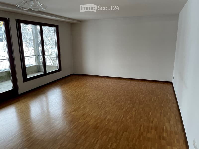 Empty room with wooden flooring, white walls, large windows, and a chandelier.