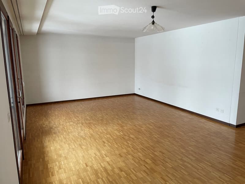 Empty room with wooden flooring, white walls, and a hanging light fixture.