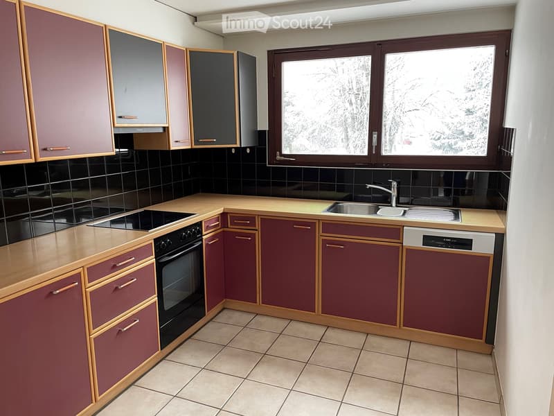 Modern kitchen with wooden countertops, maroon cabinets, black tiles, and stainless steel appliances including an oven, sink, and dishwasher.