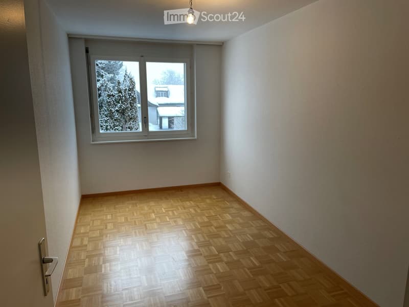 Empty room with wooden parquet flooring, white walls, and a large window showing a snowy outdoor scene.