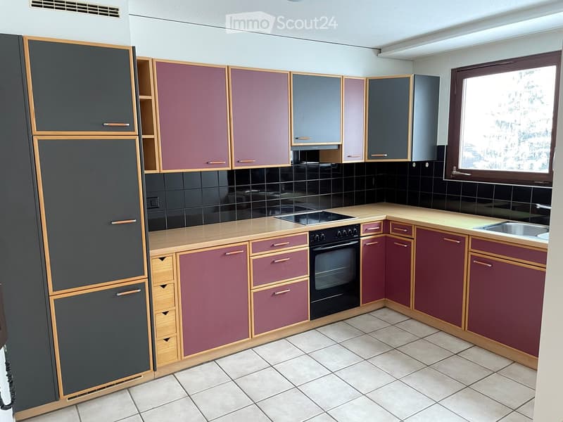 Modern kitchen with dark purple and grey cabinets, light wooden countertops, and tiled flooring.
