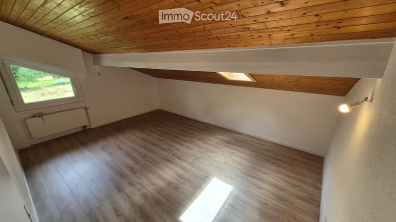 Empty attic room with wooden ceiling, wooden flooring, and a single window letting in natural light. The room is unfurnished and has a simple, clean design.
