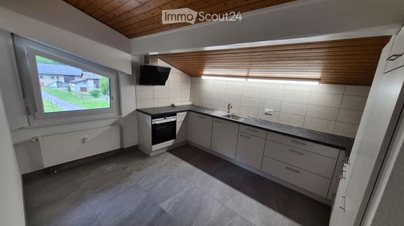 Modern kitchen with white cabinets, dark countertops, built-in oven, and a window overlooking a green area.