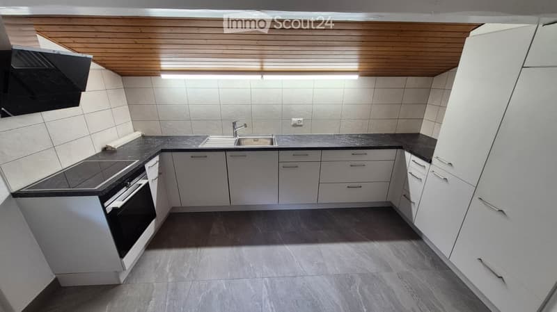 Modern kitchen with white cabinets, black countertop, stainless steel sink, and built-in oven. Wooden ceiling with integrated lighting.