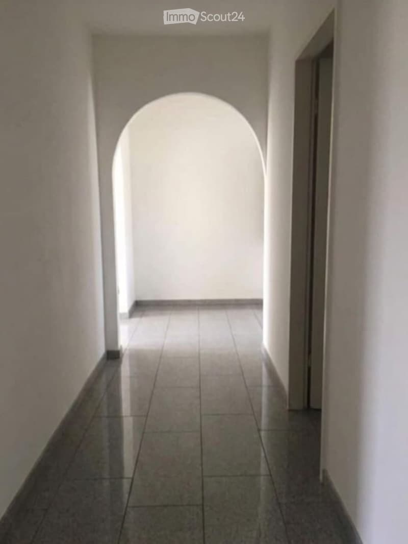 A narrow hallway with tiled flooring and an arched opening at the end, leading to a bright area.