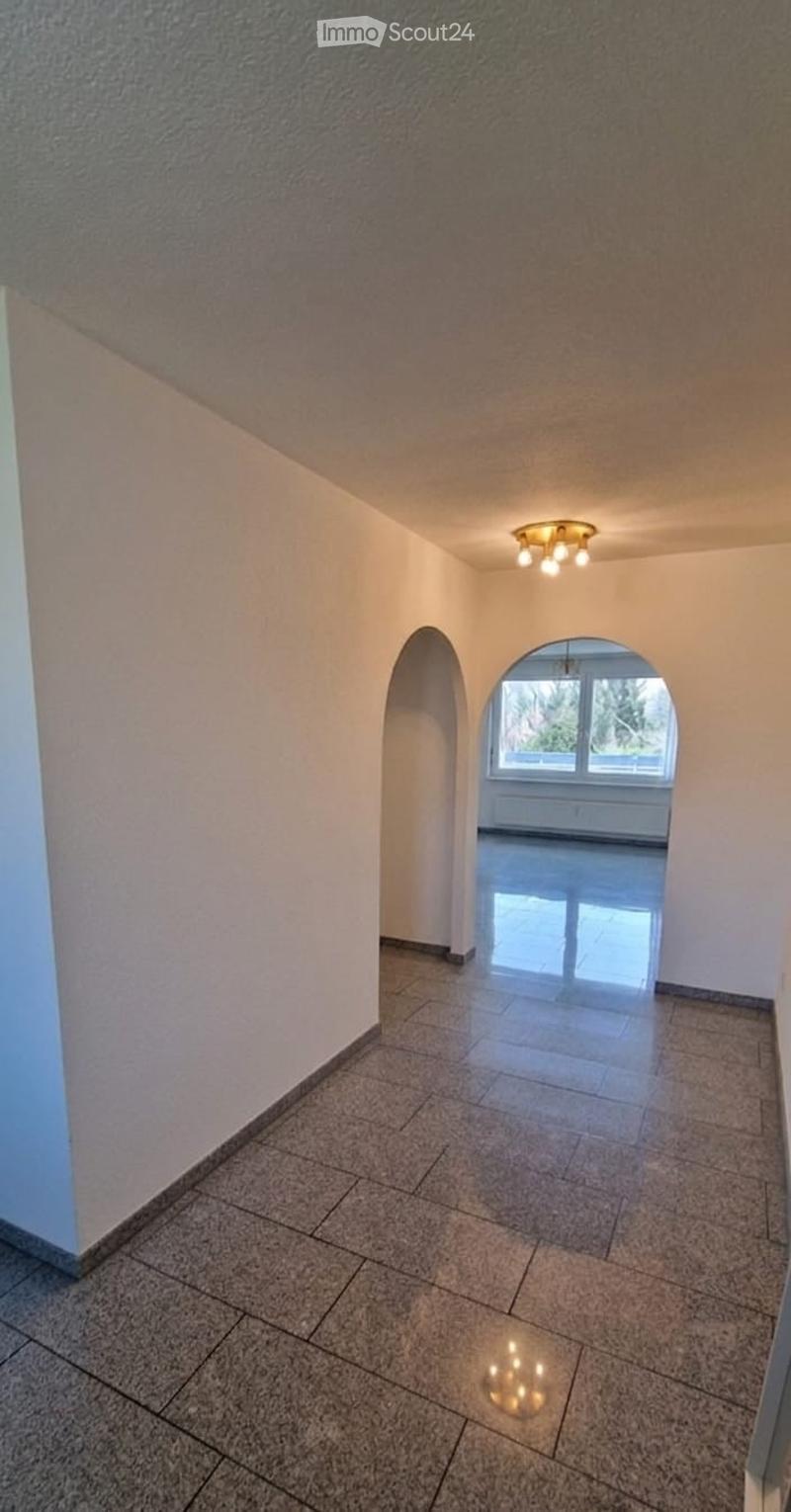 A clean, well-lit hallway with tiled flooring and arched doorways leading to another room. The walls are painted in neutral tones, and the ceiling features a modern light fixture.