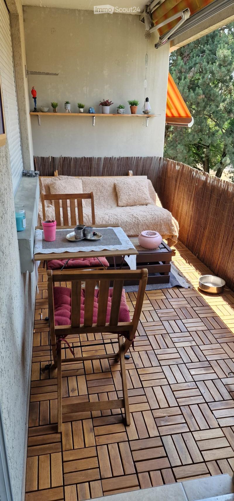 Balcony with wooden decking, sofa, small table, chairs, and potted plants.