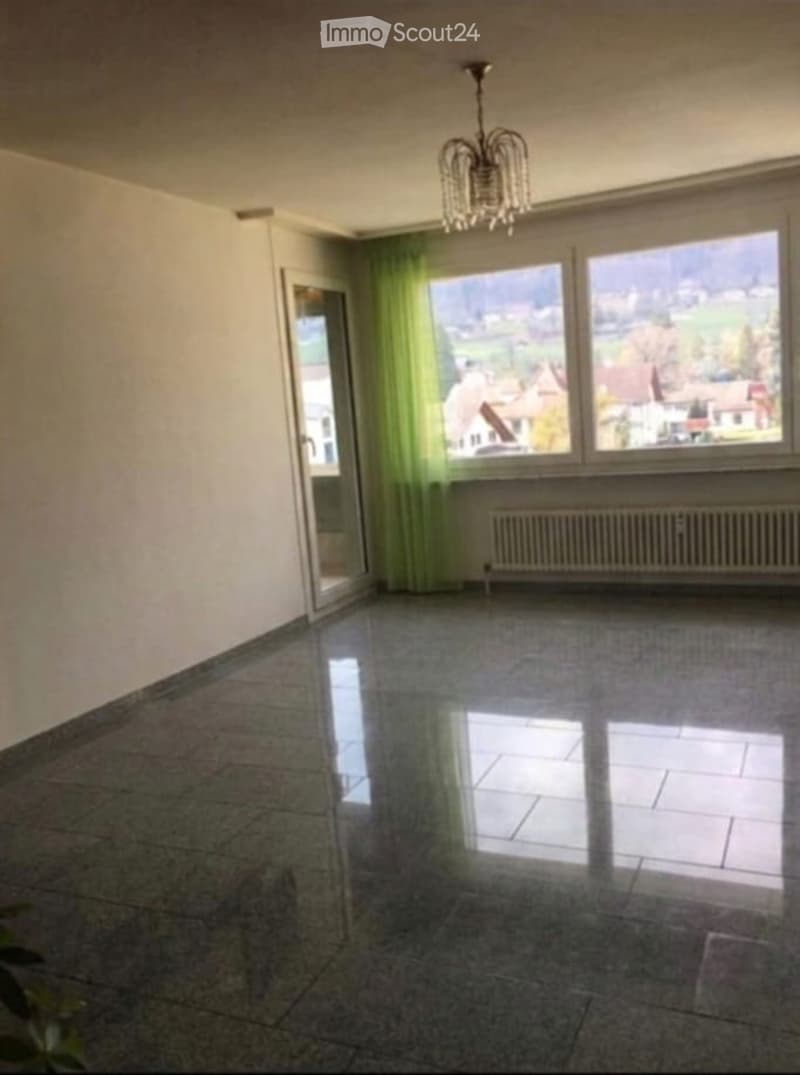 Empty room with large windows offering a scenic view, tiled floor, and a chandelier hanging from the ceiling.