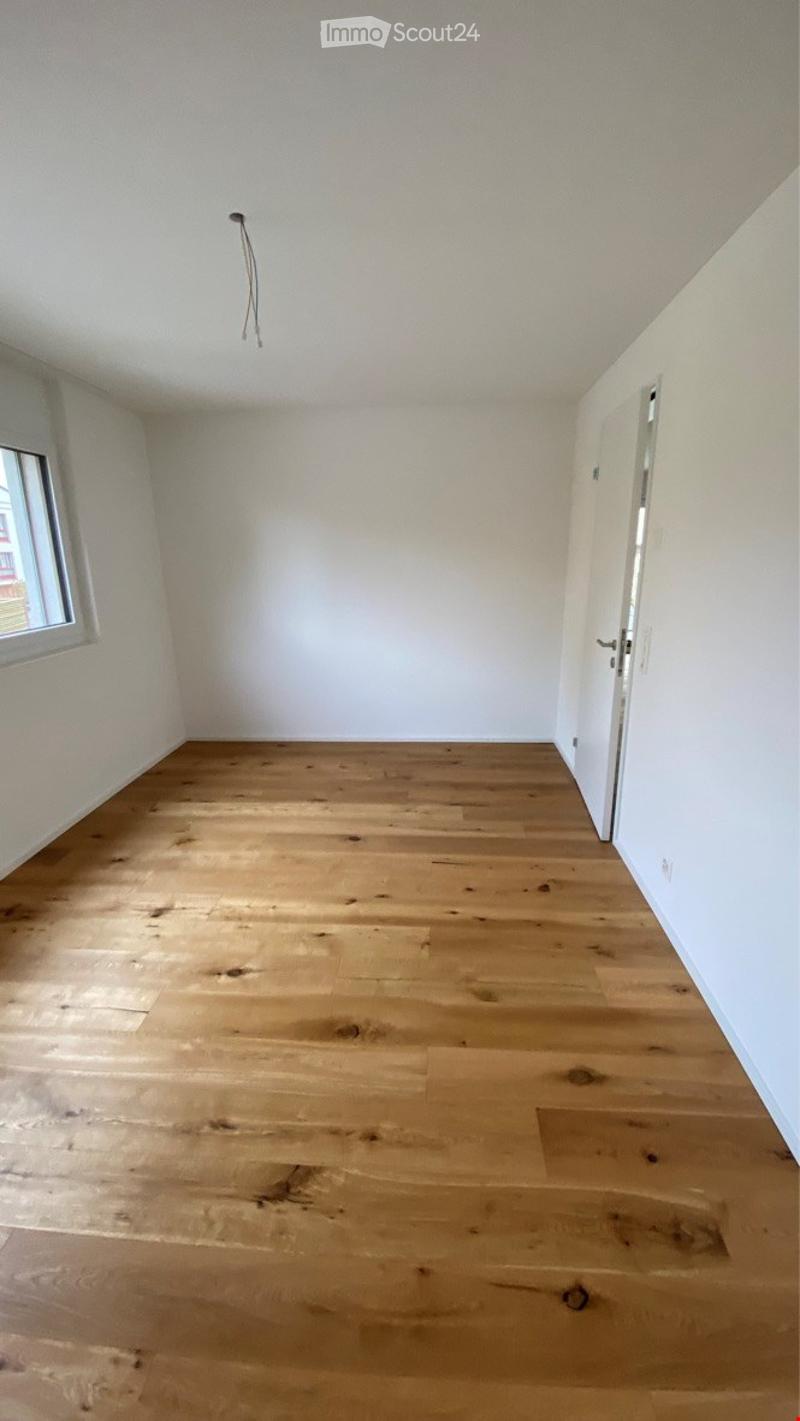 Empty room with light wooden flooring, white walls, and a single window on one side.