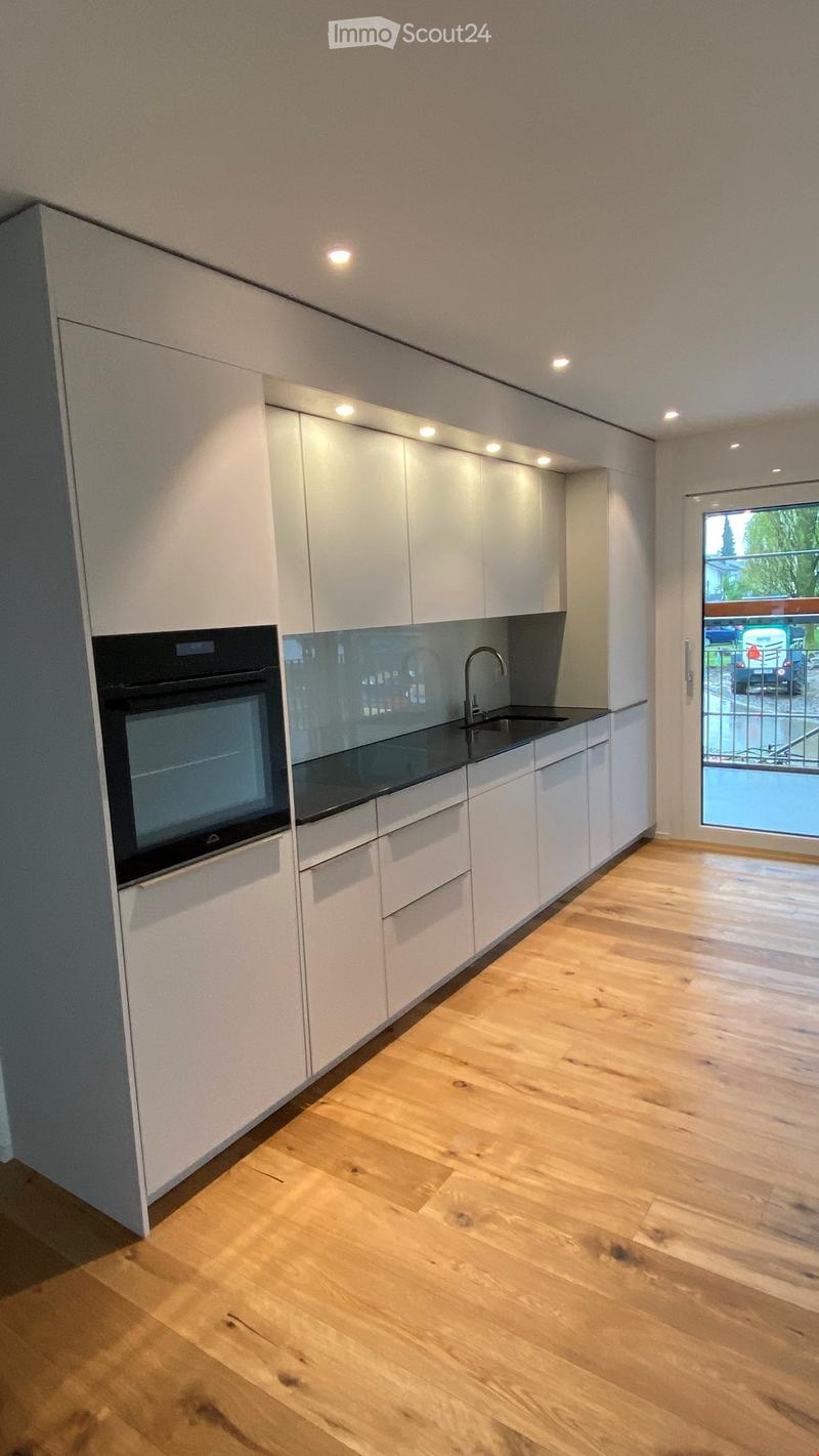 Modern kitchen with white cabinets, wooden flooring, and a black countertop. Features an oven, sink, and faucet.