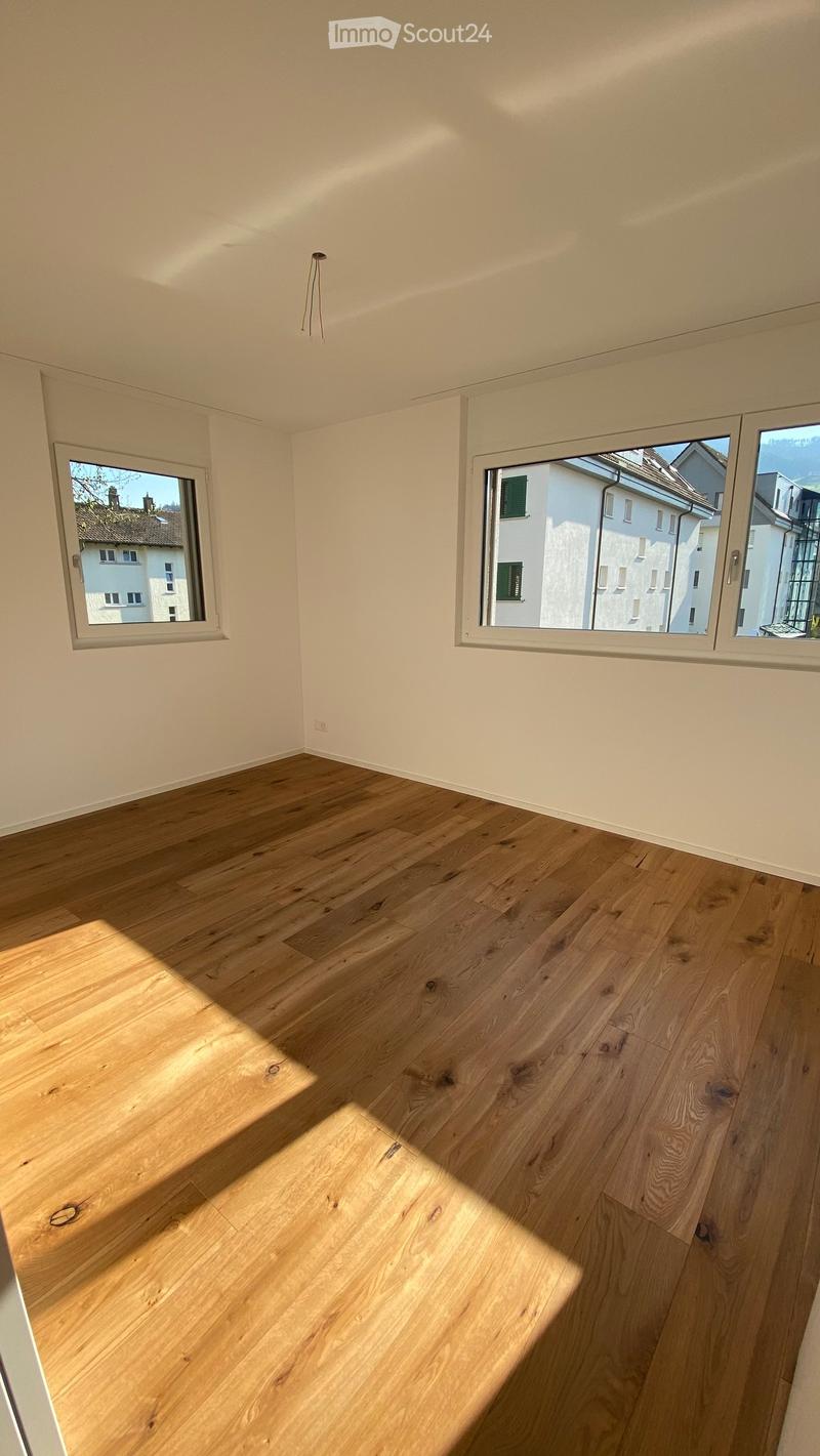Empty room with light wooden flooring and large windows offering a view of neighboring buildings.