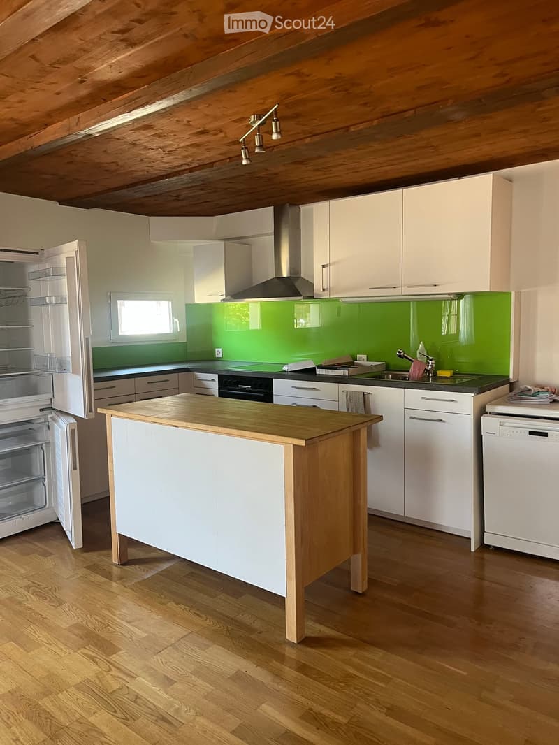 Modern kitchen with white cabinets, a wooden island, stainless steel appliances, and a green backsplash.
