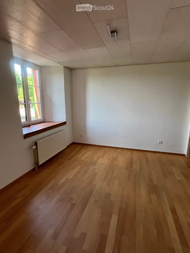 Empty room with wooden flooring, white walls, and a window with a radiator below it.