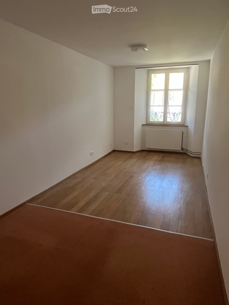 Empty room with wooden flooring, white walls, and a window with a radiator below it.