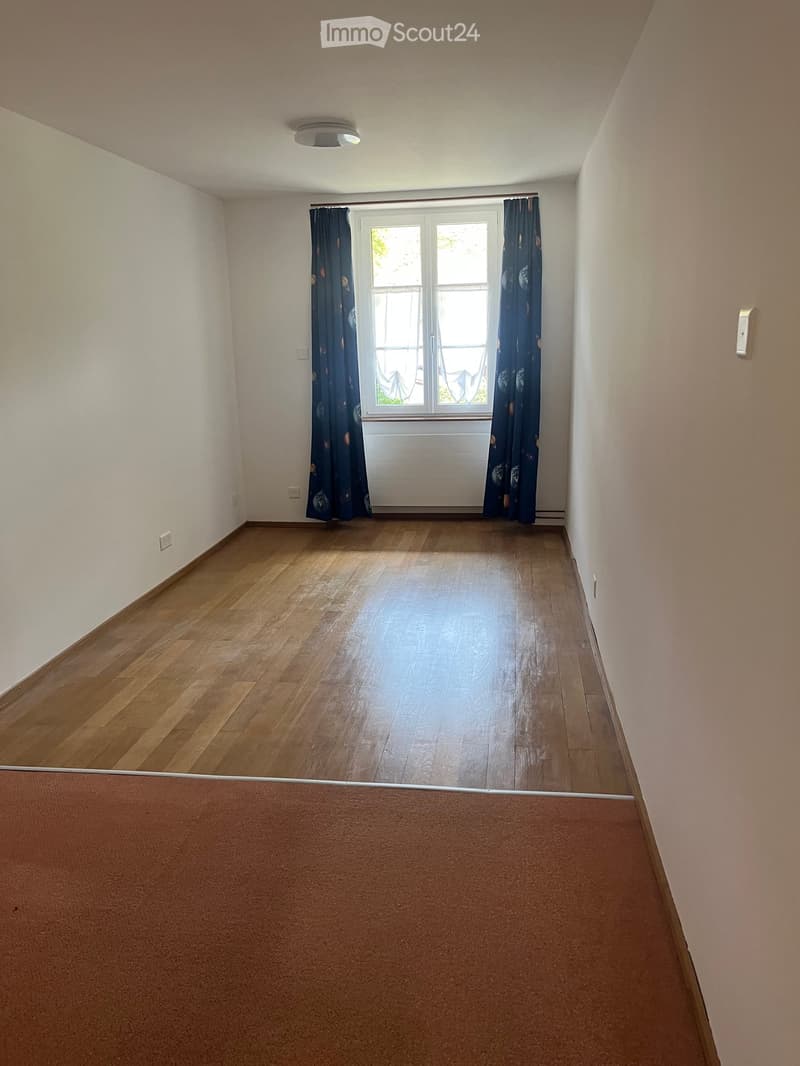 Empty room with wooden flooring, white walls, and a window with dark curtains. No furniture or equipment present.
