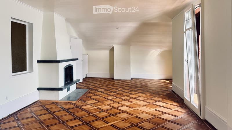Empty room with wooden parquet flooring, white walls, and a fireplace with a black mantelpiece.