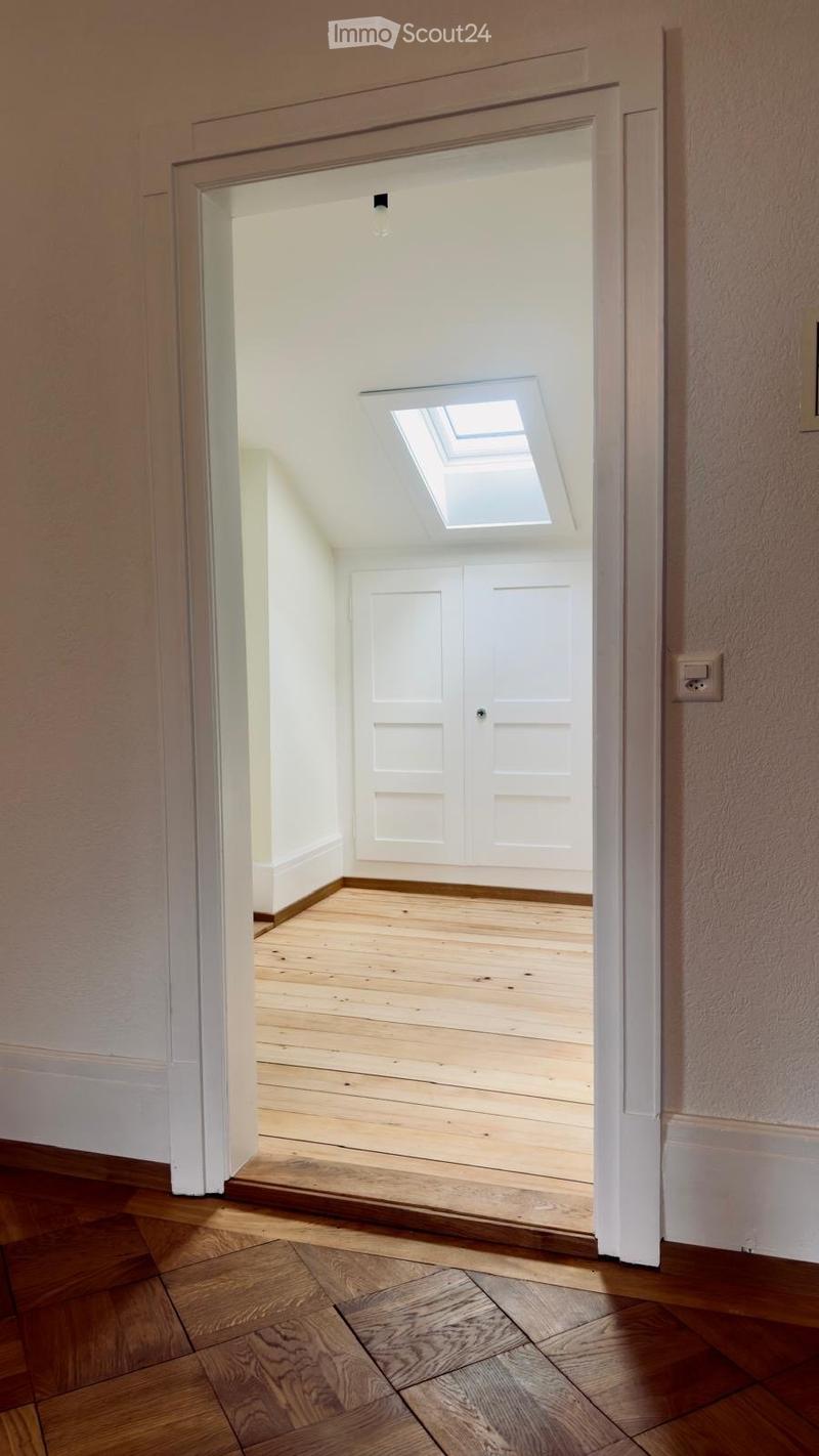 Empty hallway with wooden flooring, white walls, and a skylight above a closed white door.