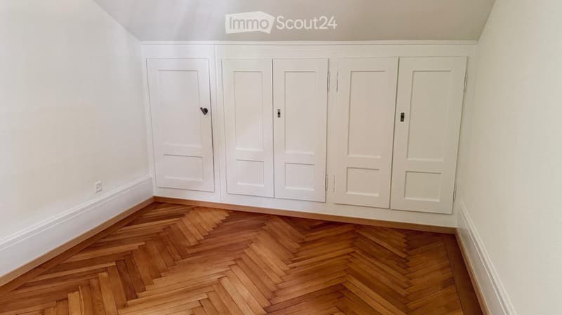 Empty room with white walls, wooden herringbone floor, and built-in white closet units.