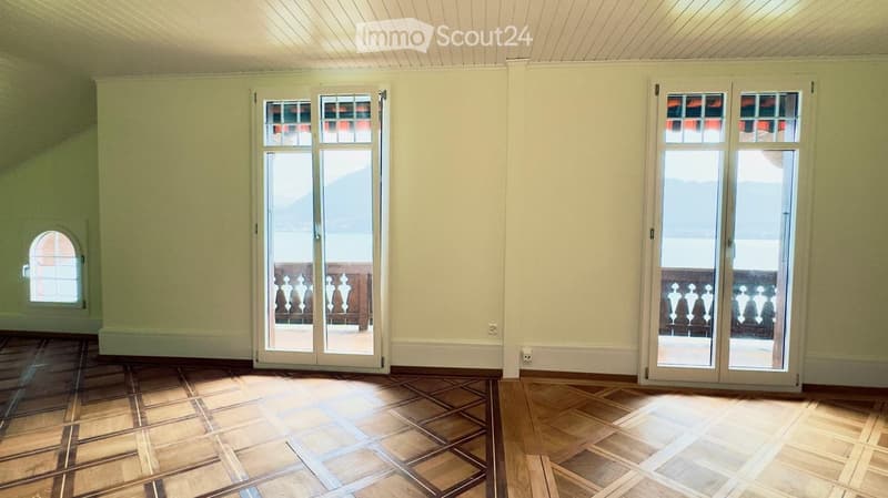 Empty room with light-colored walls, wooden flooring, and large glass doors leading to a balcony.
