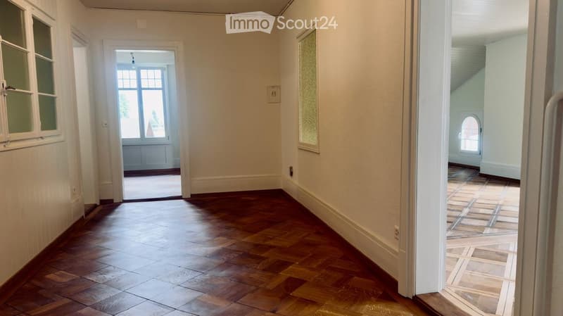 Empty hallway with wooden flooring, white walls, and several doors leading to other rooms.