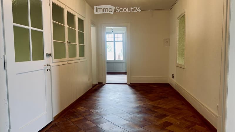 Empty hallway with wooden flooring, white walls, and a door leading to another room.