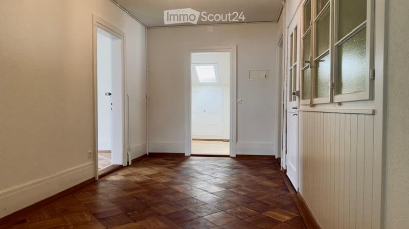 Empty hallway with wooden flooring, white walls, and multiple doors leading to other rooms.