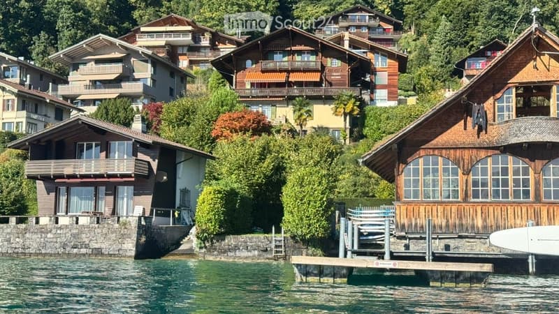 Lakeside houses, wooden exterior, multiple balconies, terraced hillside, lush greenery, water view