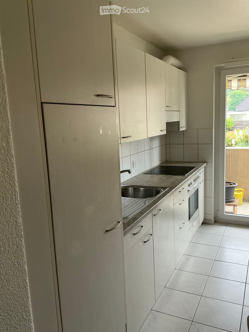 Modern kitchen with white cabinets, stainless steel appliances, and a tiled floor. Features a sink, oven, and refrigerator.