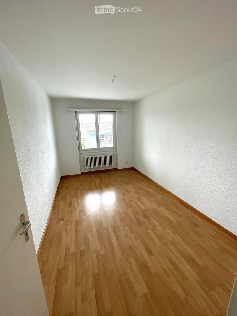 Empty room with wooden flooring, white walls, and a window with a radiator below it.