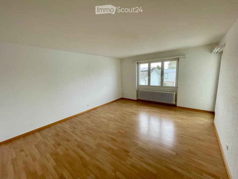 Empty room with wooden flooring, white walls, and a large window with a radiator below it.