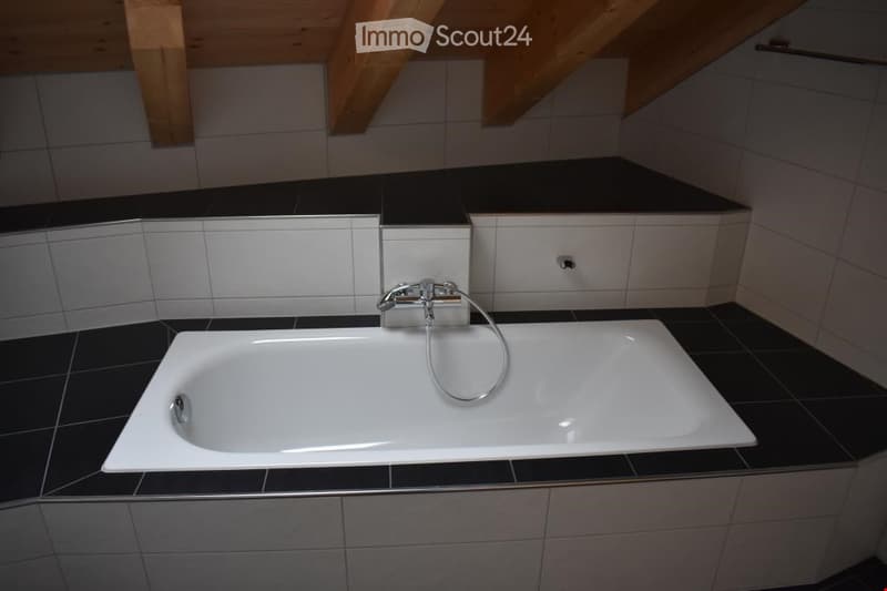 white bathtub, black tiled walls, wooden ceiling beams, silver faucet