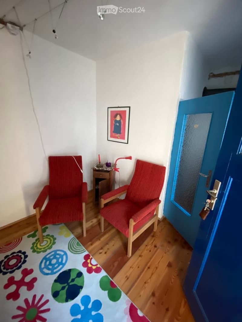 small room with two red chairs, a rug, a small table with a lamp, a picture frame on the wall, and a blue door