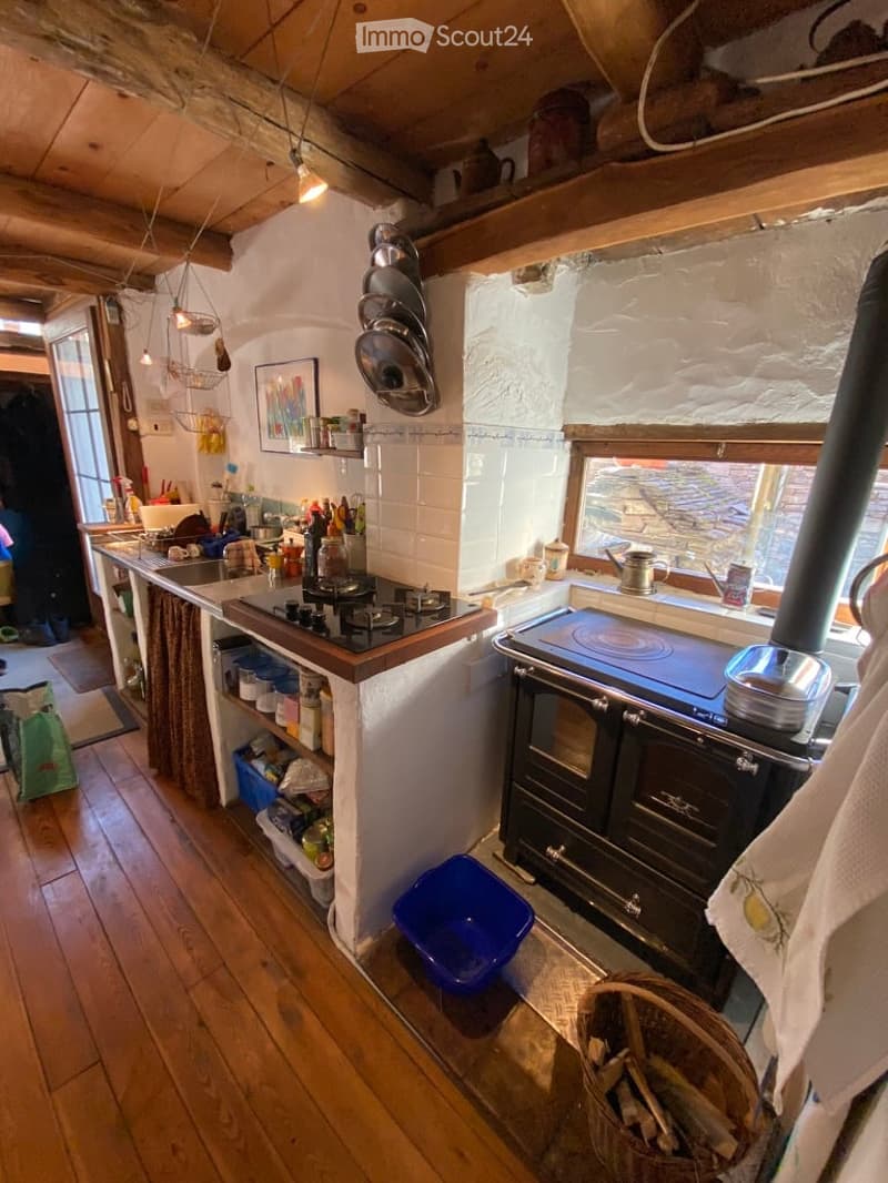 kitchen with wooden floor, white walls, gas stove, oven, sink, shelves, hanging pots, window, fireplace