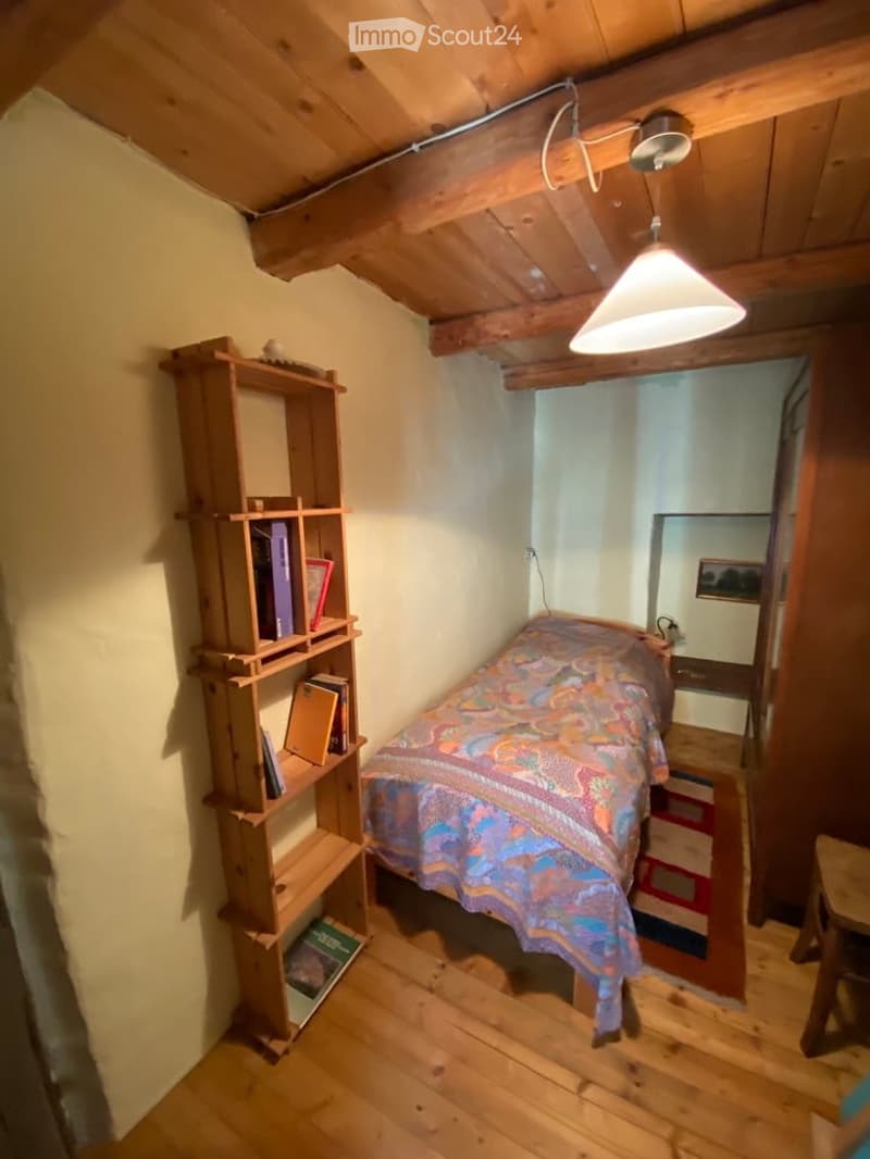 small bedroom with bed, wooden shelf, wooden floor, wooden ceiling, lamp, picture frame