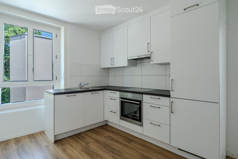 Modern kitchen with white cabinets, stainless steel appliances, and wooden flooring.
