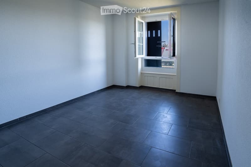 Empty room with dark tiled floor, white walls, and an open window with a view of the outside.