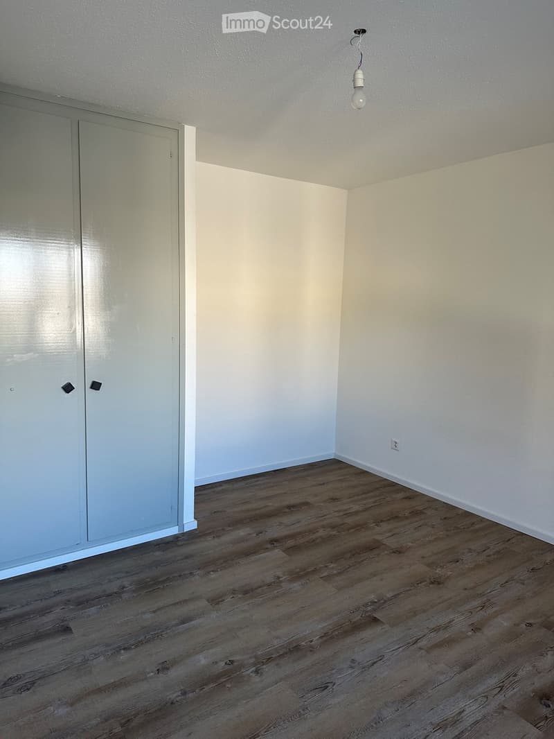 Empty room with light-colored walls, wooden flooring, and a single door. No furniture or equipment is present.