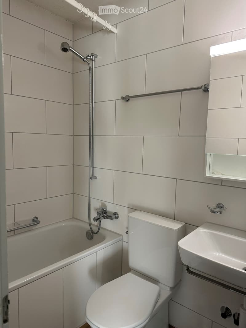 Modern bathroom with white tiles, bathtub, toilet, sink, and showerhead.