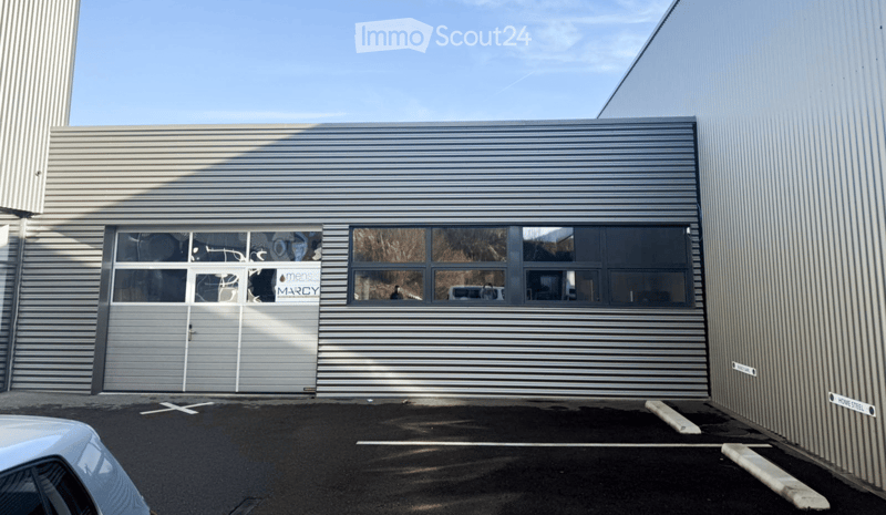 Modern industrial-style building with a large garage door and multiple windows, featuring a sleek metallic exterior and a clear blue sky in the background.