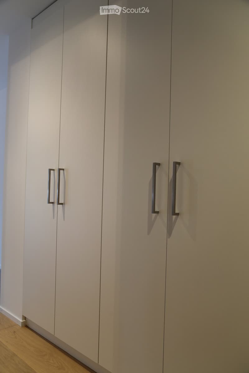 Empty room with light-colored built-in wardrobes and modern handles, wooden flooring, and white walls.