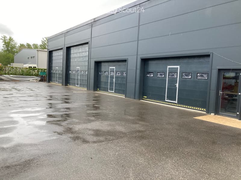 A large industrial building with multiple garage doors and a wet parking area in front.