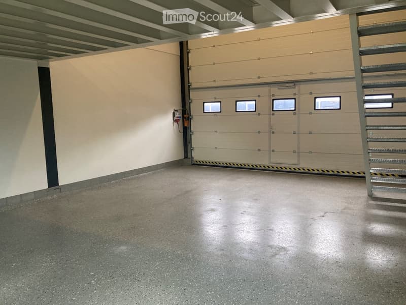 Empty underground garage with concrete floor, beige walls, and multiple garage doors with small windows.