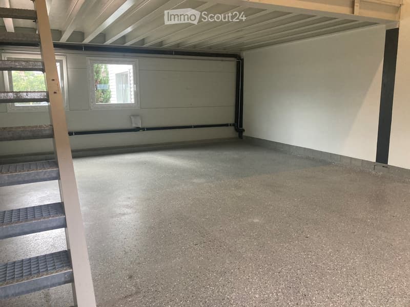 Empty garage with concrete floor, metal staircase, and small window showing greenery outside.