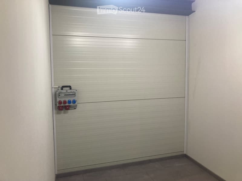 Empty room with a closed garage door and a control panel featuring red and blue switches.