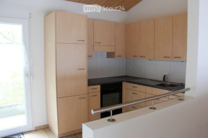 Modern kitchen with light wooden cabinets, black countertop, and stainless steel sink.