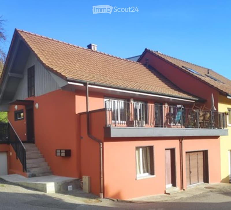 Two-story house with red-tiled roof, orange exterior, white trim, and a balcony with metal railing.