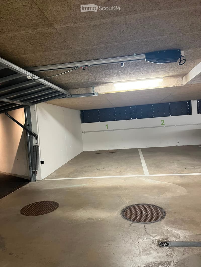 Underground garage with concrete floor, white walls, numbered parking spaces, and two manhole covers.