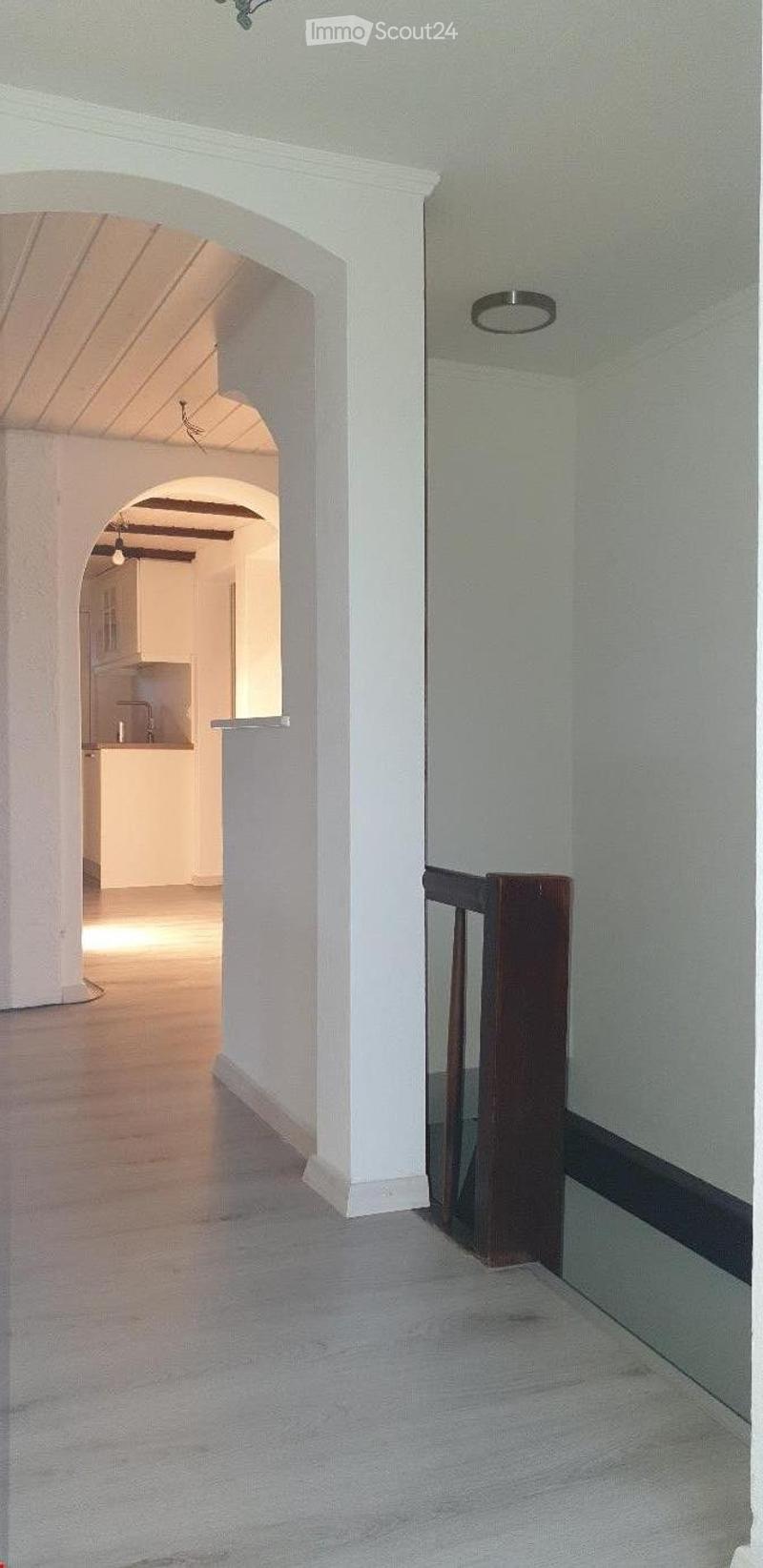 Bright, open hallway with white walls, wooden flooring, and arched doorways leading to other rooms.