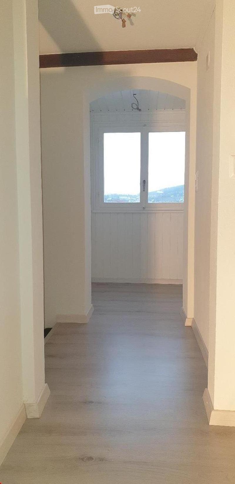 Empty hallway with white walls, carpeted floor, and a large window at the end.