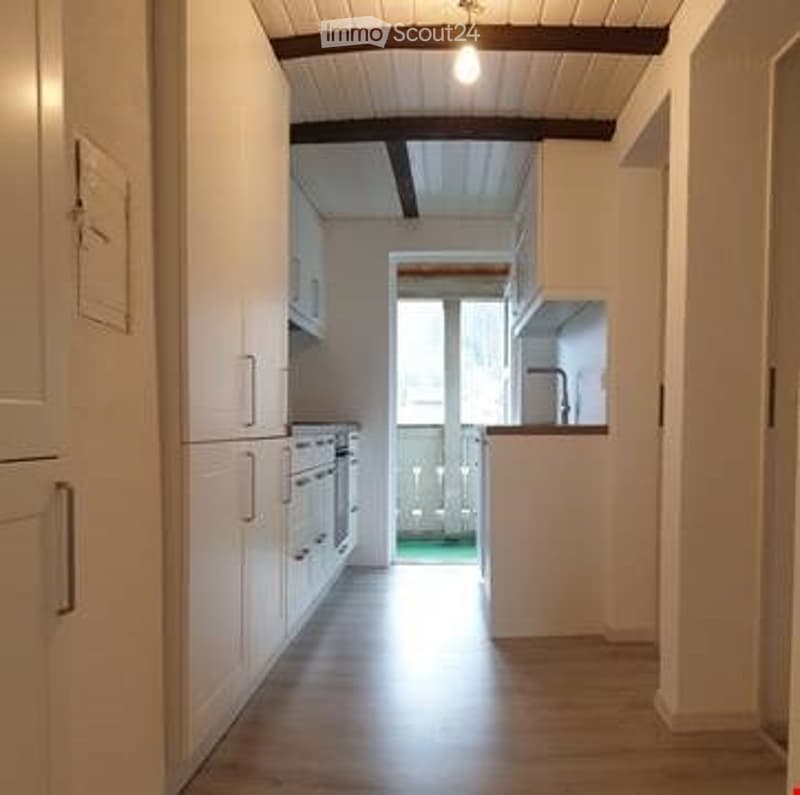 Empty kitchen with white cabinets, wooden floor, and a small window with a view of a balcony area.